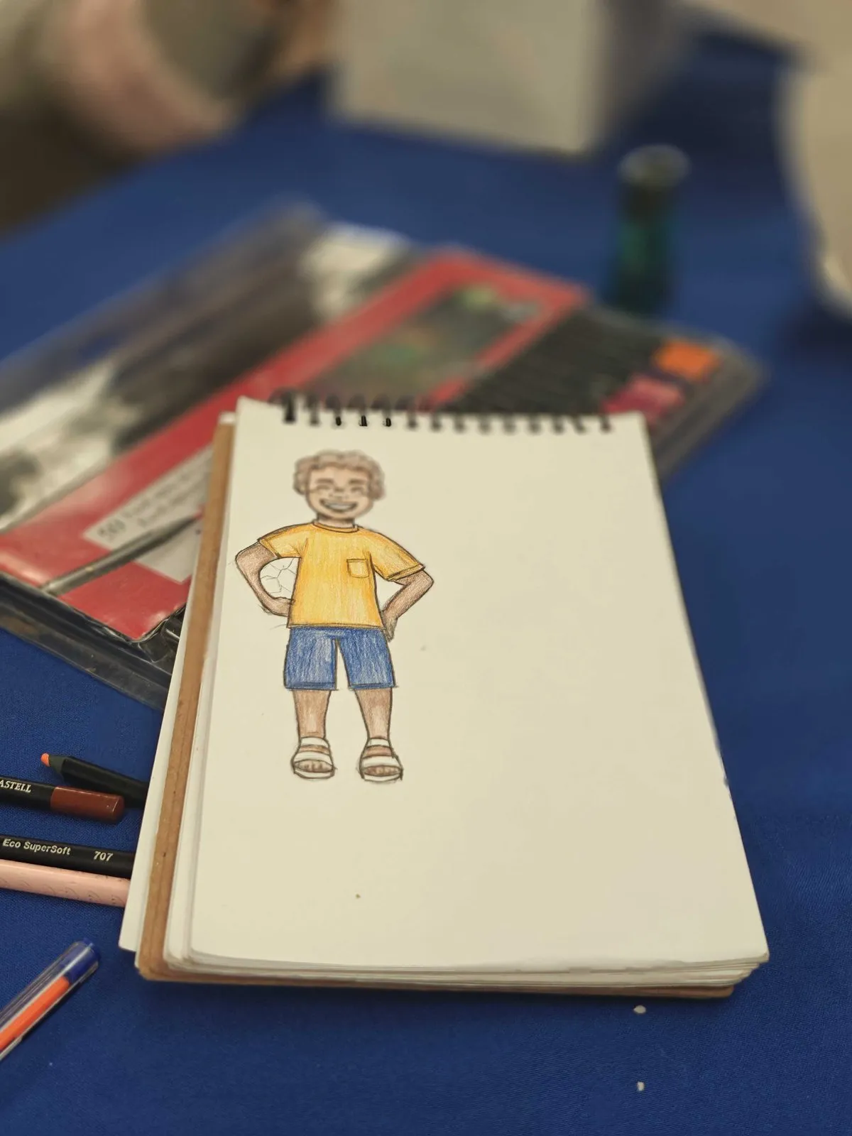 Un cuaderno con el boceto de un personaje, junto a lápices de colores.